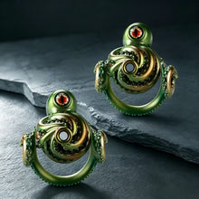 Load image into Gallery viewer, Two Abyssal Eye Alloy Chastity Cages displayed from the front on a dark stone surface
